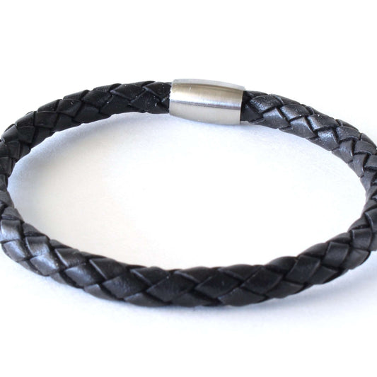 Black braided leather bracelet with a cylindrical stainless-steel clasp, displayed in a circular shape to highlight its woven texture and minimalist design.