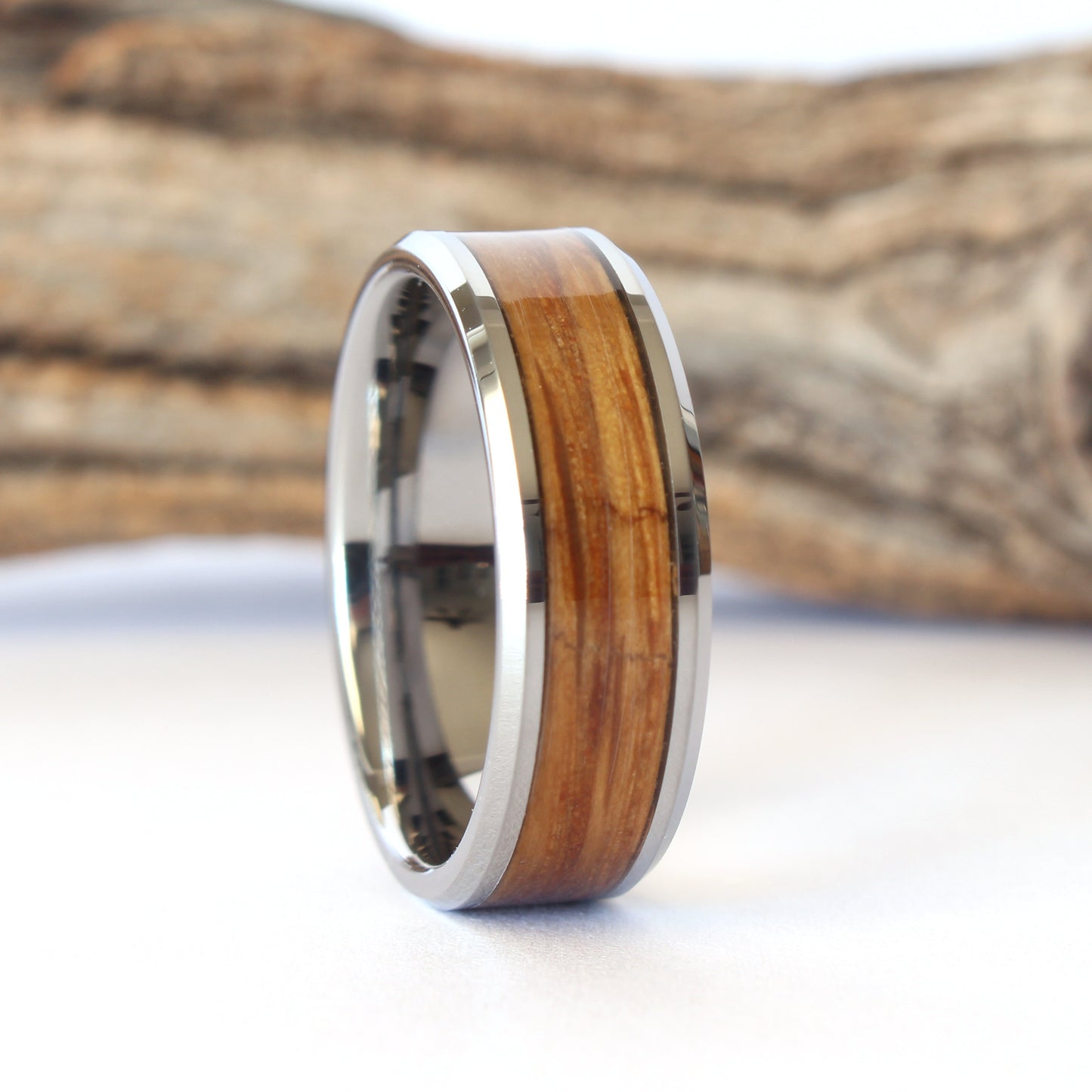 A tungsten ring with whiskey barrel wood inlay, displayed against a wooden background.