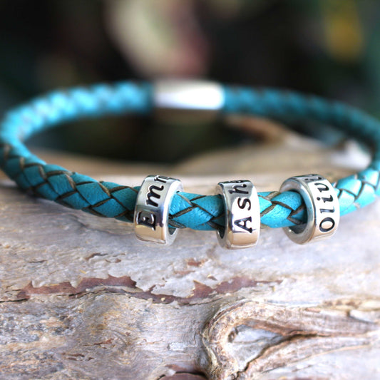 Braided turquoise leather bracelet with three sterling silver engraved name beads reading Emma, Asher, and Olivia, finished with a secure metallic clasp.
