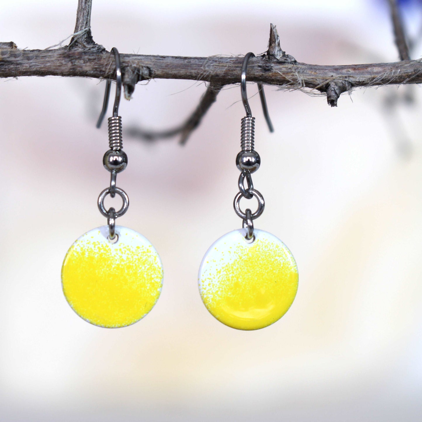Gradient white yellow disc earrings hanging from a branch with a neutral background