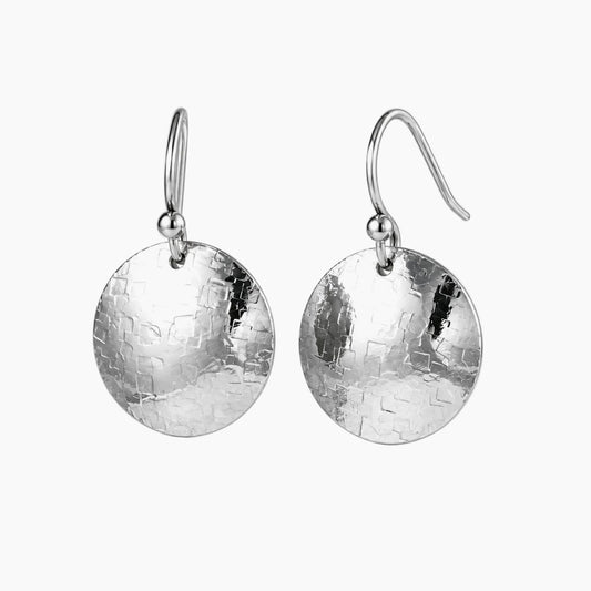 A pair of silver drop earrings with hammered circular disc pendants and fishhook wires, shown on a light gray background.