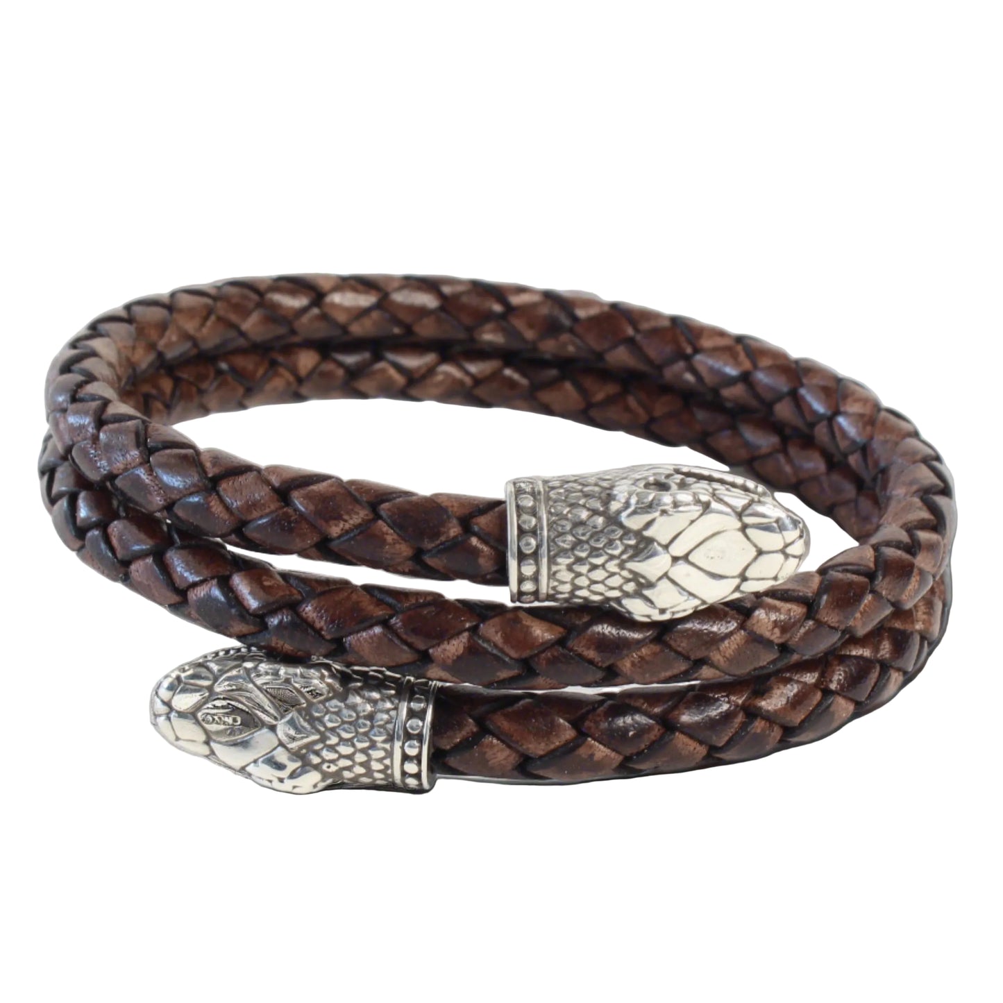 Handcrafted braided leather bracelet in dark brown, coiled in a circle with two silver snake head end pieces featuring detailed scales and facial features. The design blends rugged texture with intricate metalwork, highlighting artisanal craftsmanship.