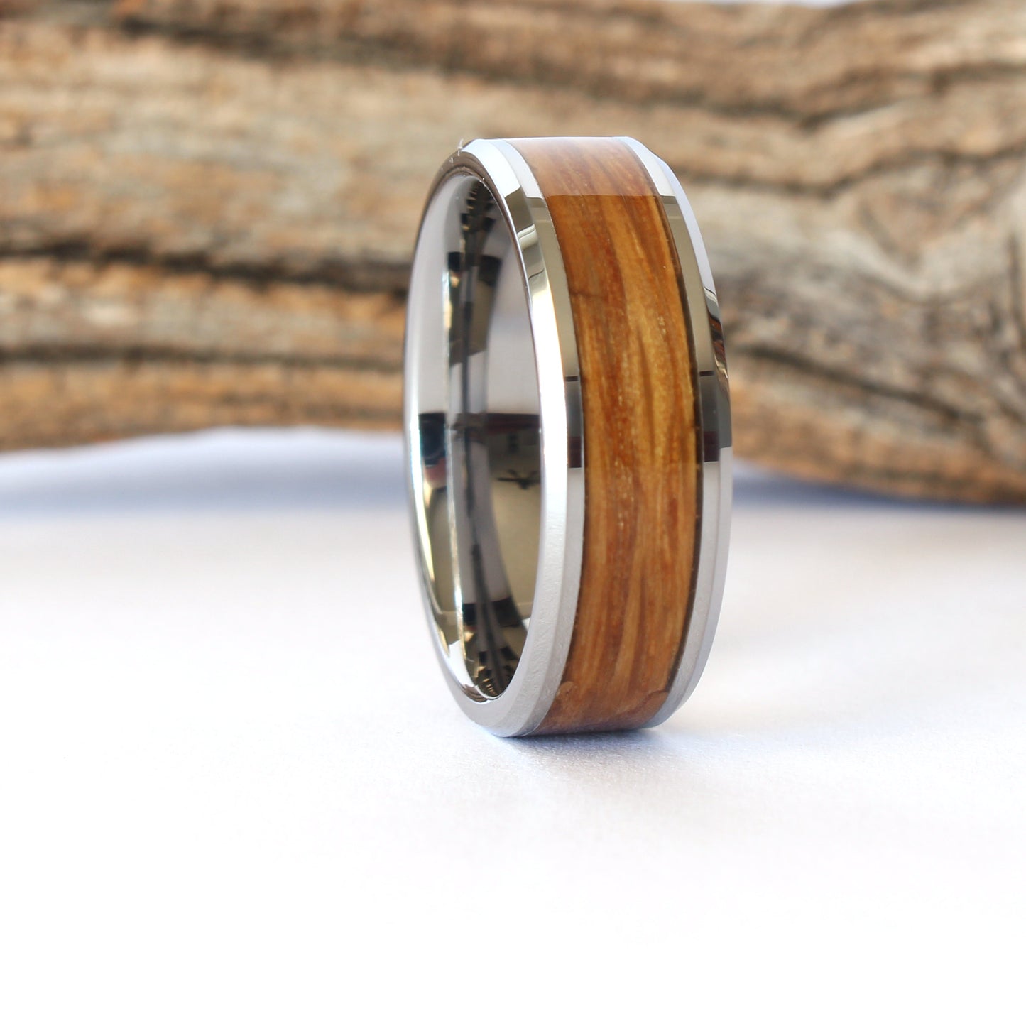 A tungsten ring with whiskey barrel wood inlay, displayed against a wooden background.