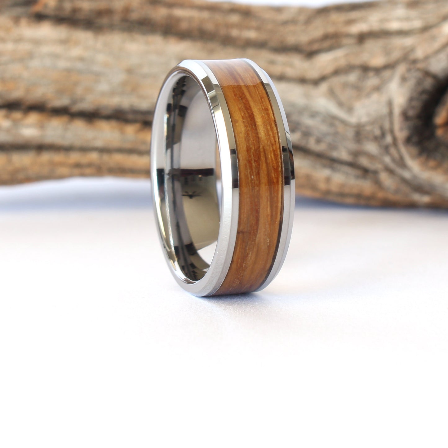 A tungsten ring with whiskey barrel wood inlay, displayed against a  white and wooden background.