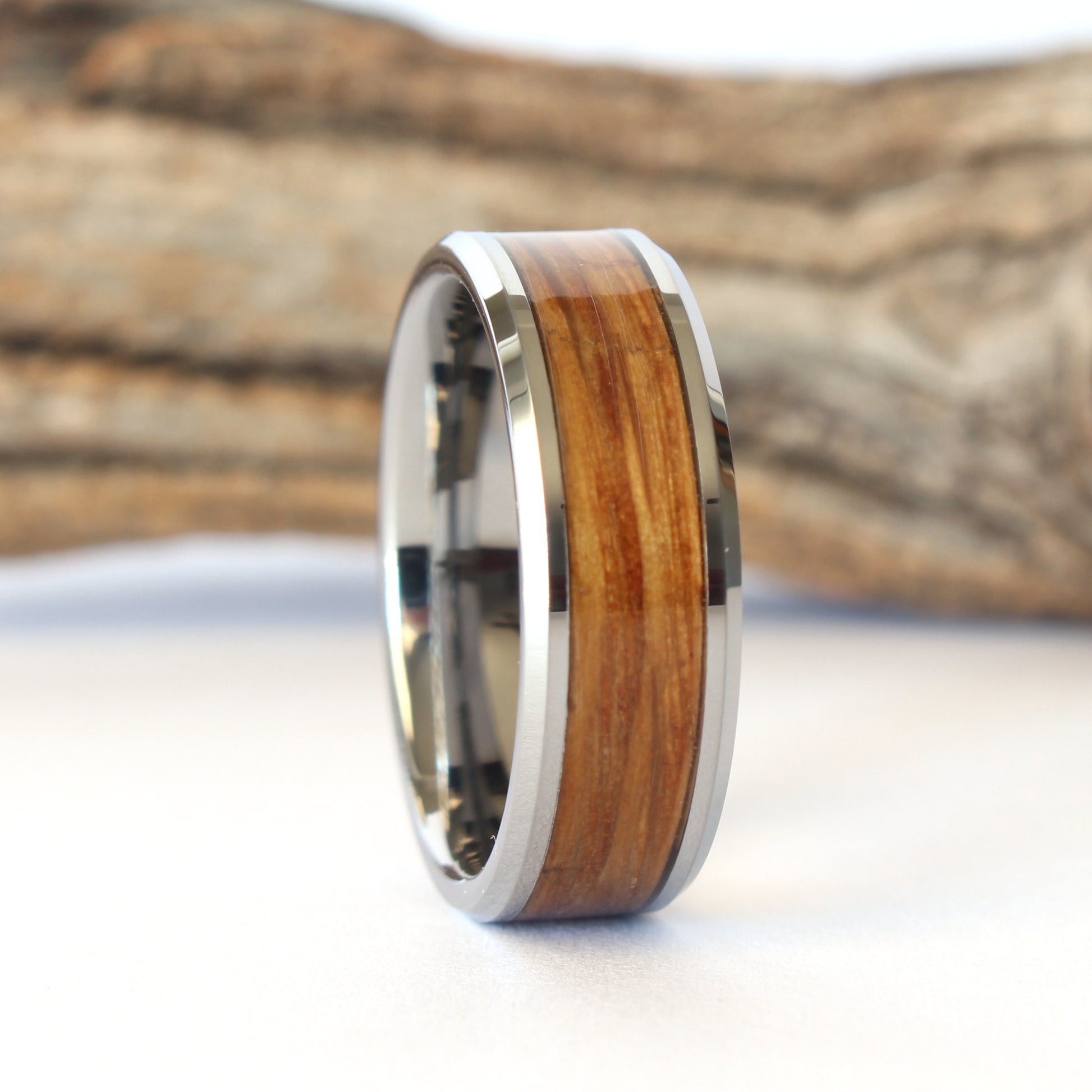 A tungsten ring with whiskey barrel wood inlay, displayed against a wooden background.
