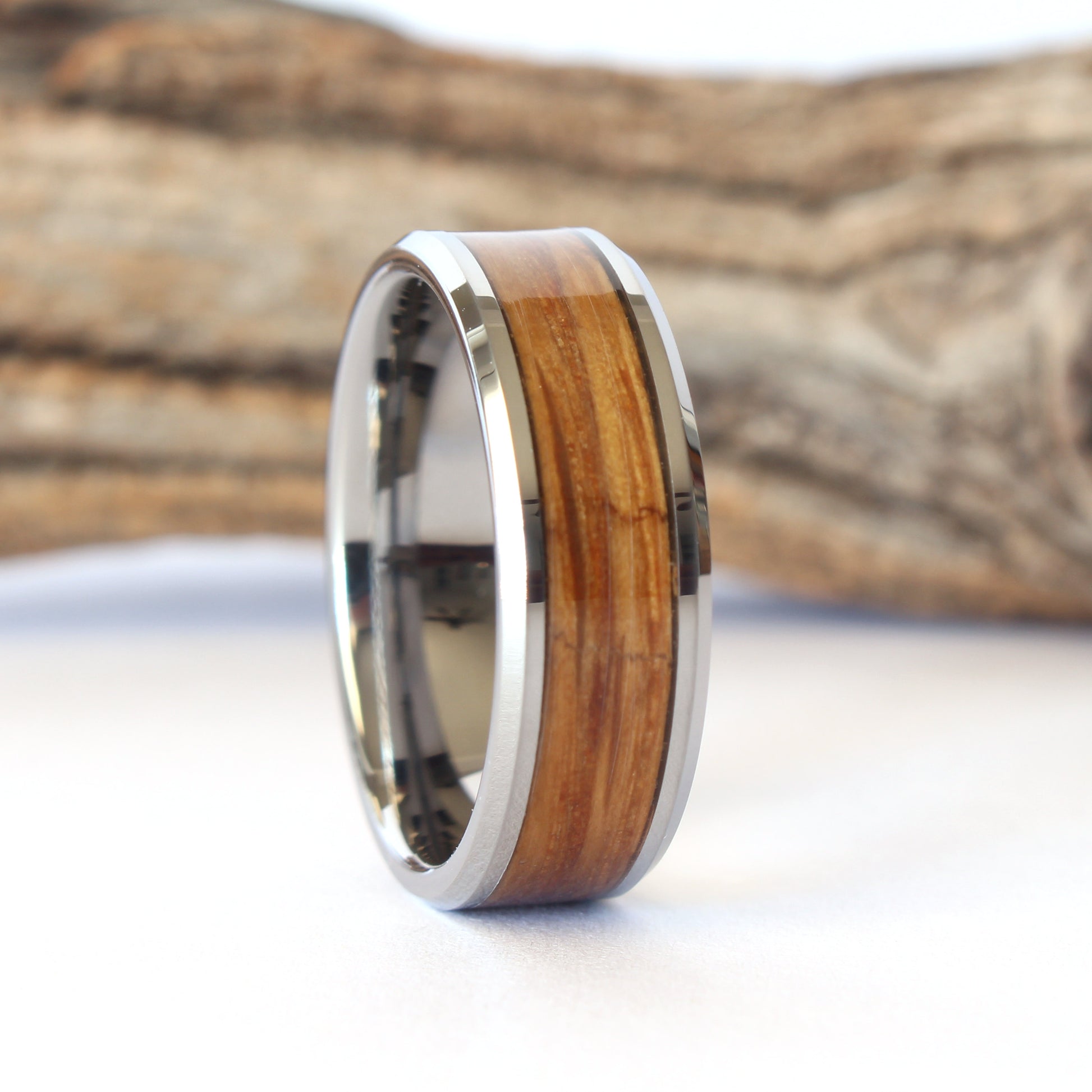 A tungsten ring with whiskey barrel wood inlay, displayed against a wooden background.