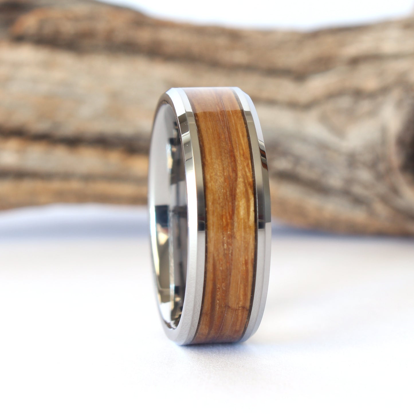 A tungsten ring with whiskey barrel wood inlay, displayed against a wooden background.