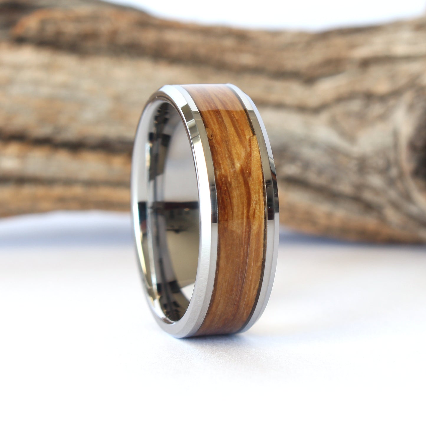 A tungsten ring with whiskey barrel wood inlay, displayed against a wooden background.
