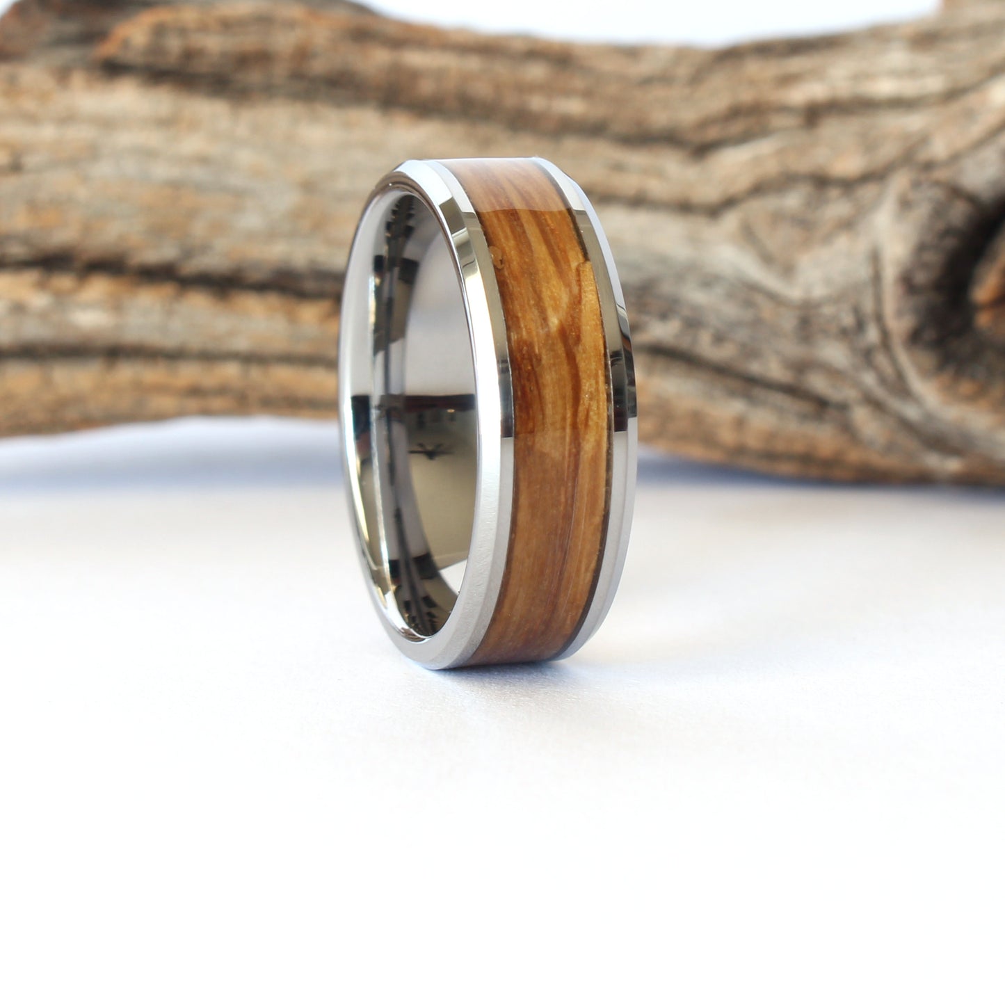 A tungsten ring with whiskey barrel wood inlay, displayed against a wooden background.
