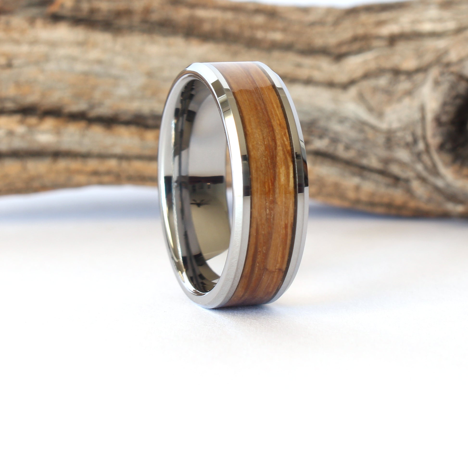 A tungsten ring with whiskey barrel wood inlay, on a white surface with a wooden background