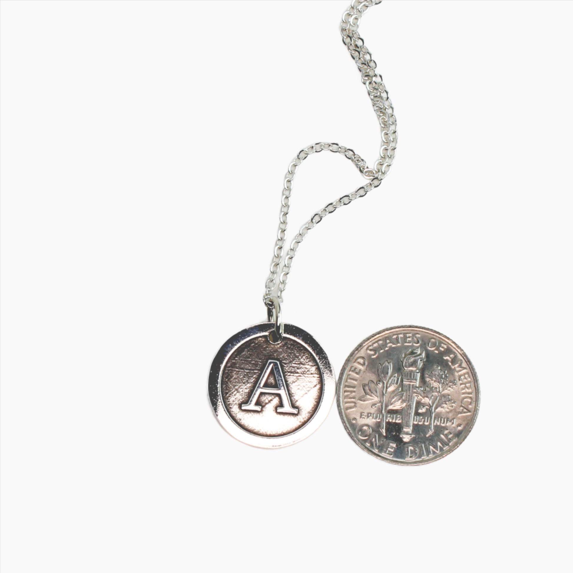 Sterling Silver Initial Necklace Beside a Dime to Show Size on a White Background
