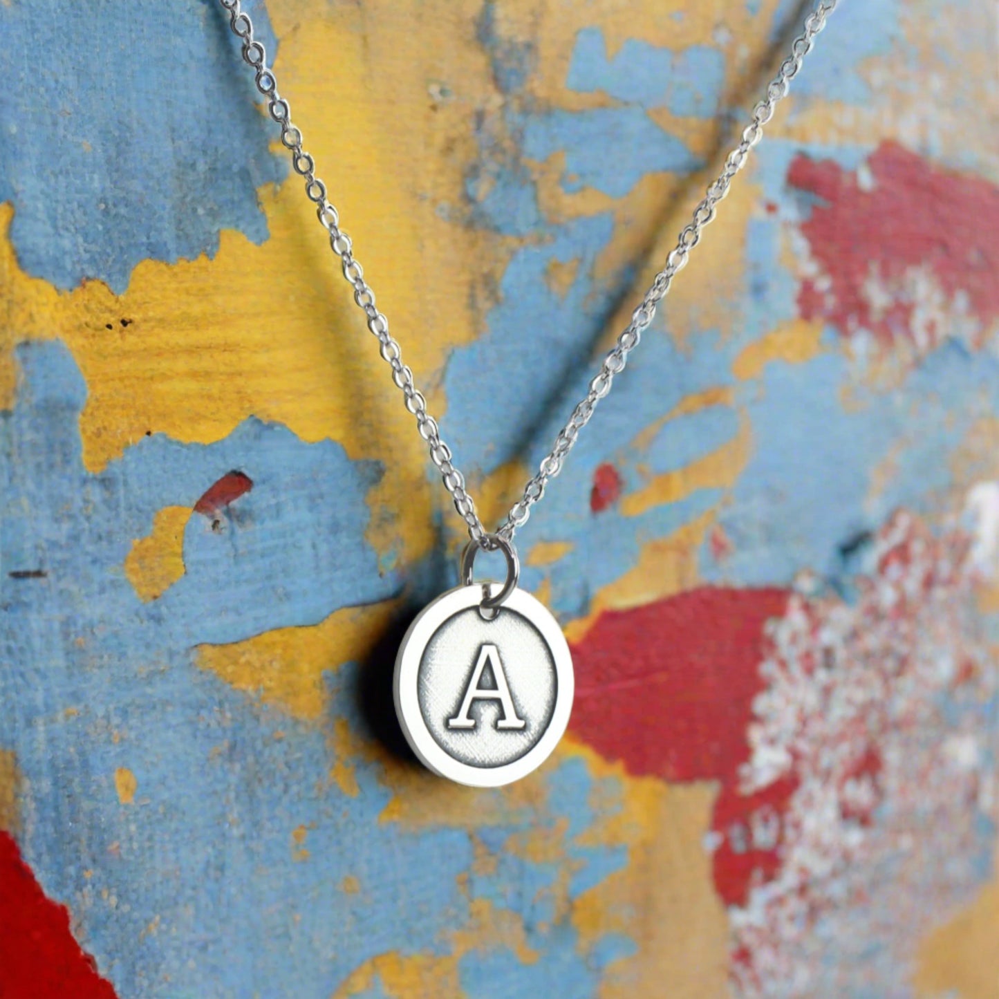 Sterling Silver Initial Necklace against a blue, yellow and red background